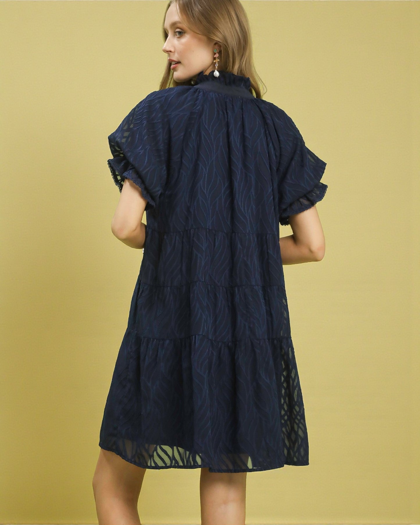 Woman wearing a navy blue dress with lace details on a yellow background