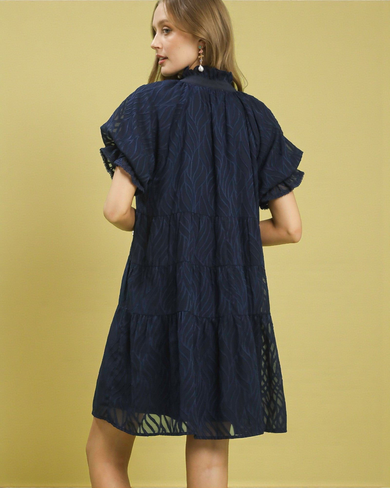 Woman wearing a navy blue dress with lace details on a yellow background