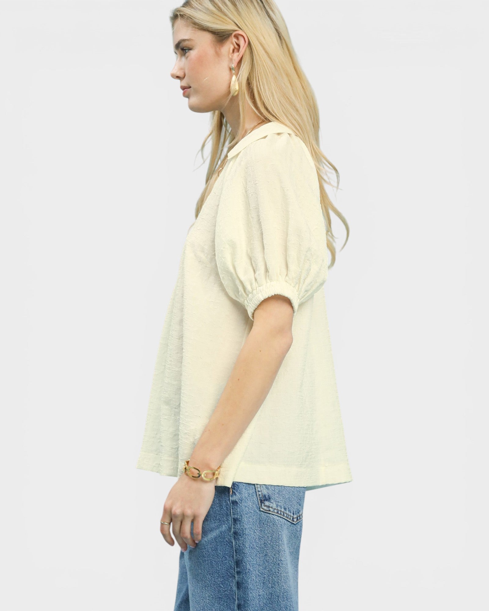 Woman wearing a light yellow blouse and blue jeans on a plain background