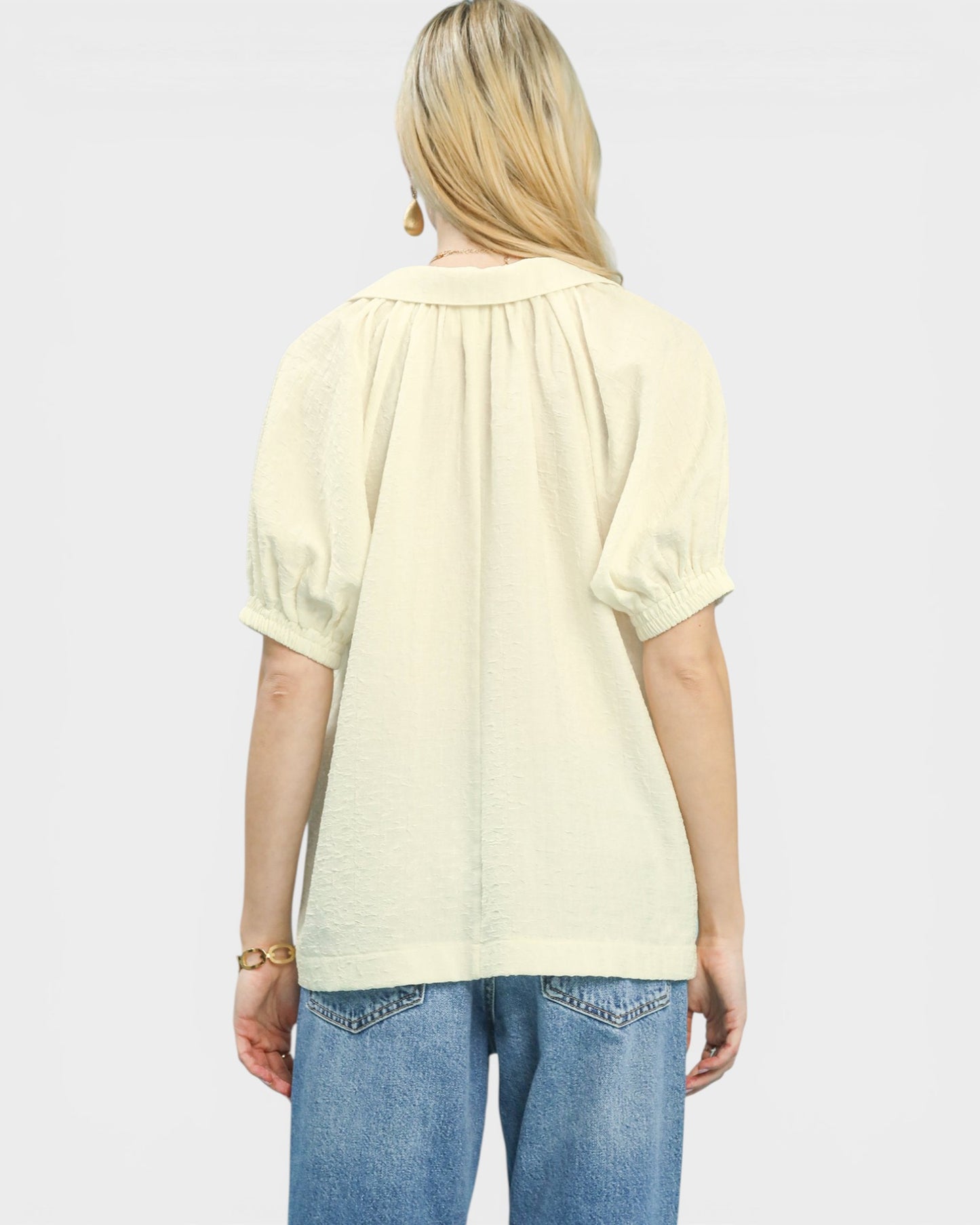 Person wearing a light yellow blouse and blue jeans on a white background