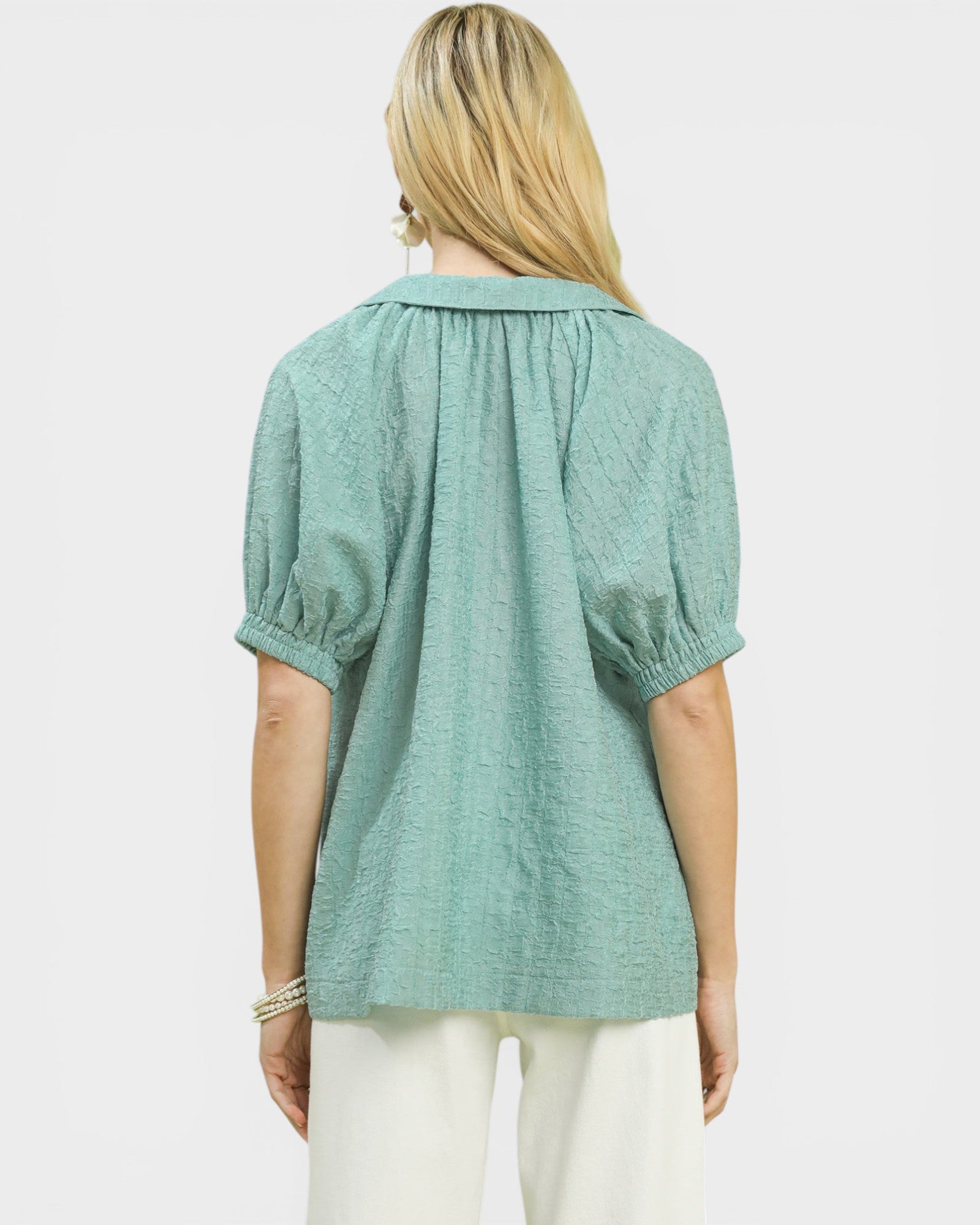 Person wearing a light green blouse with puff sleeves on a white background