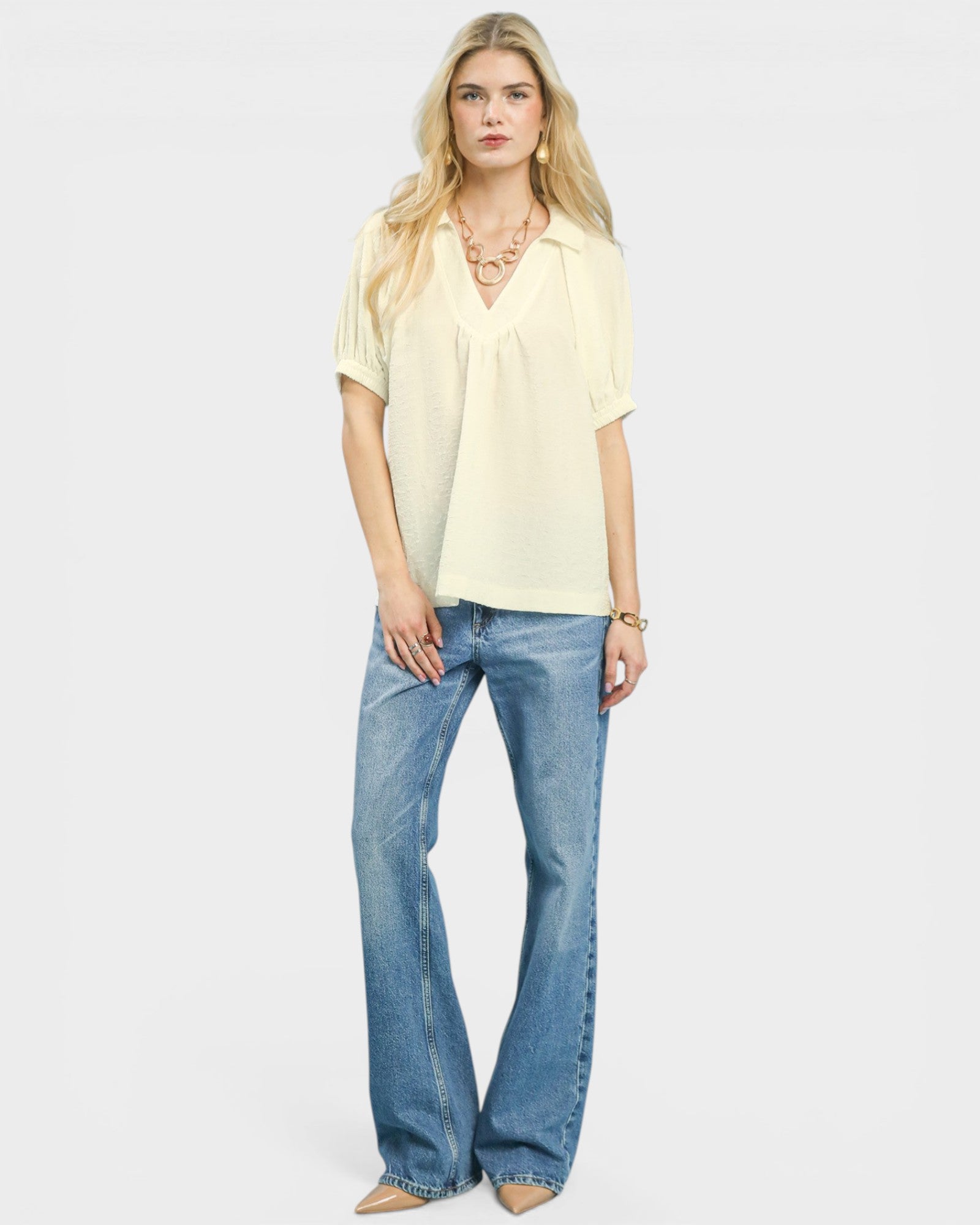 Woman wearing a light yellow top and blue jeans on a white background
