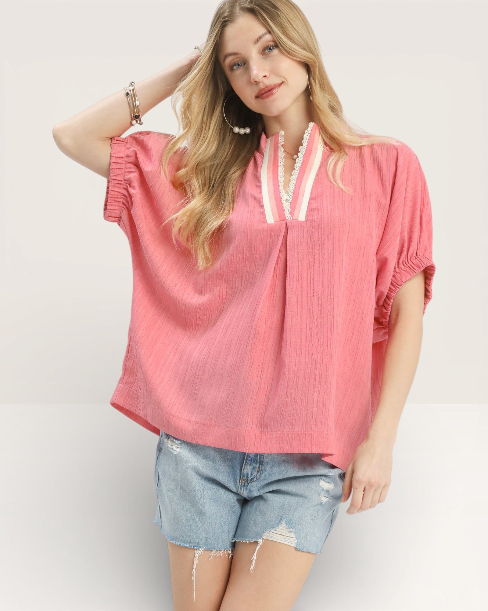 Woman wearing a pink blouse with ruffled sleeves and denim shorts on a white background