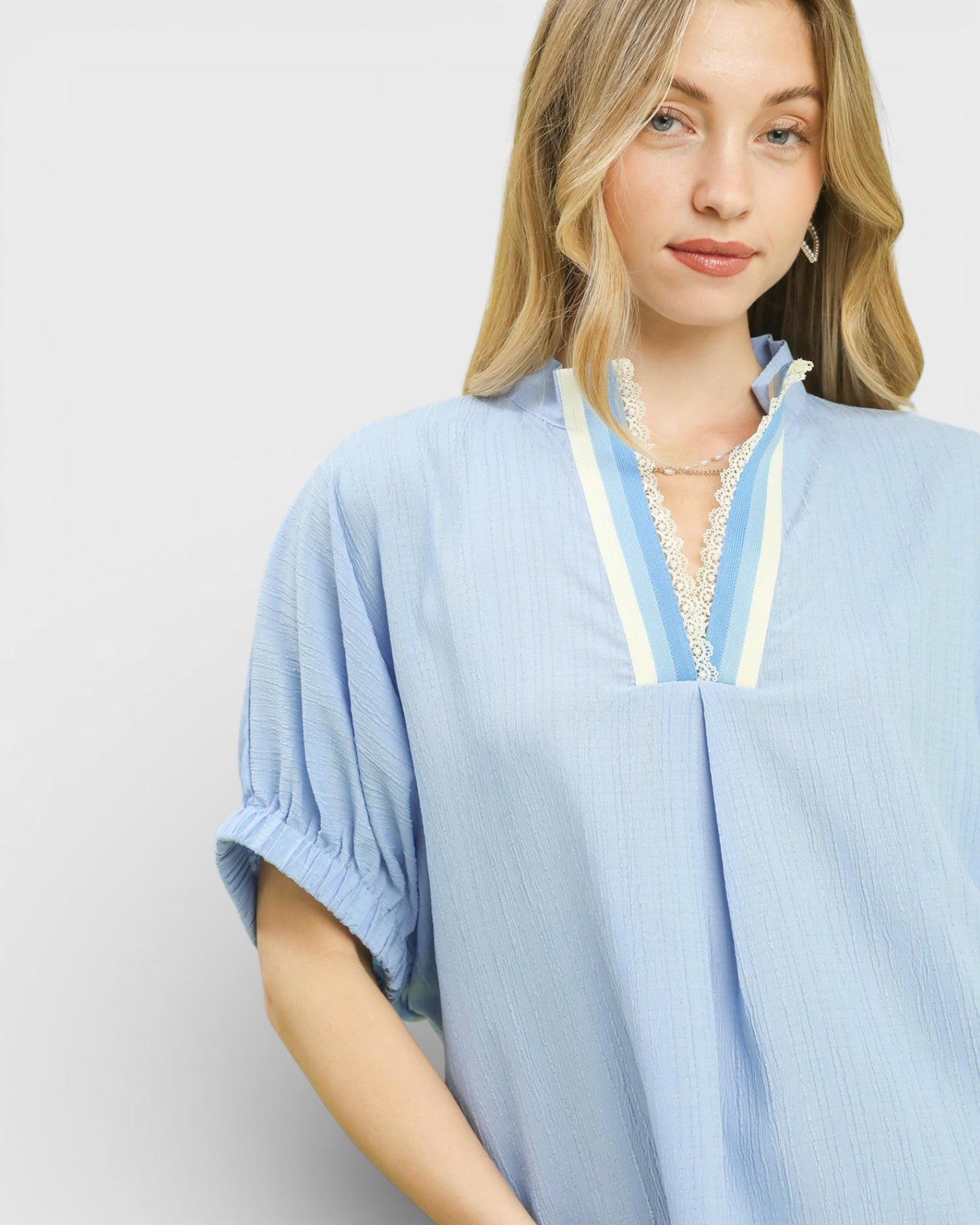 Woman wearing a light blue kimono-style garment with lace trim on a plain background