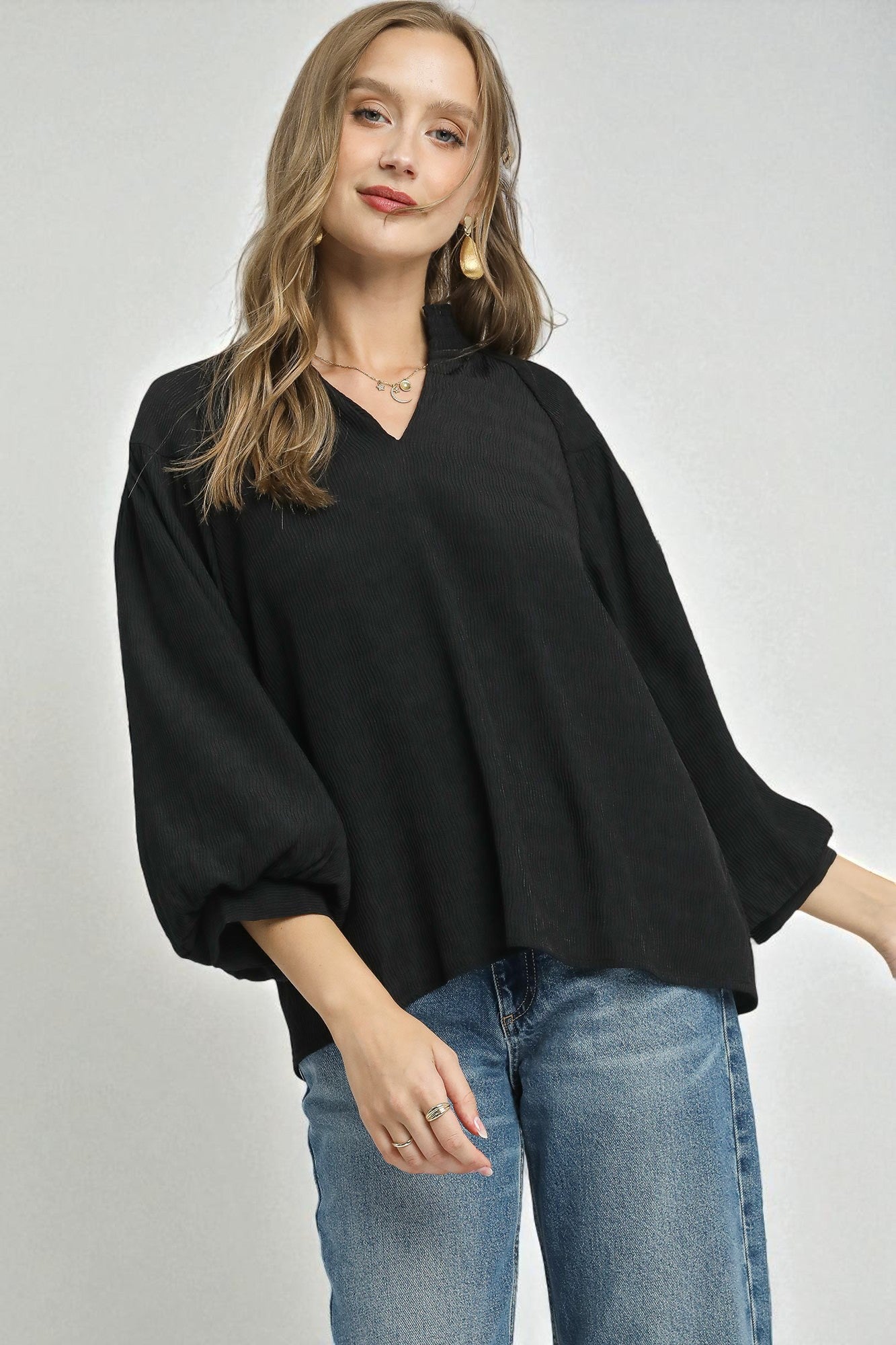 Woman wearing a black top and blue jeans on a plain background