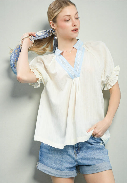 Woman wearing a white blouse with blue trim and denim shorts against a gray background