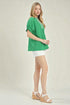 Woman wearing a green blouse and white shorts on a plain background