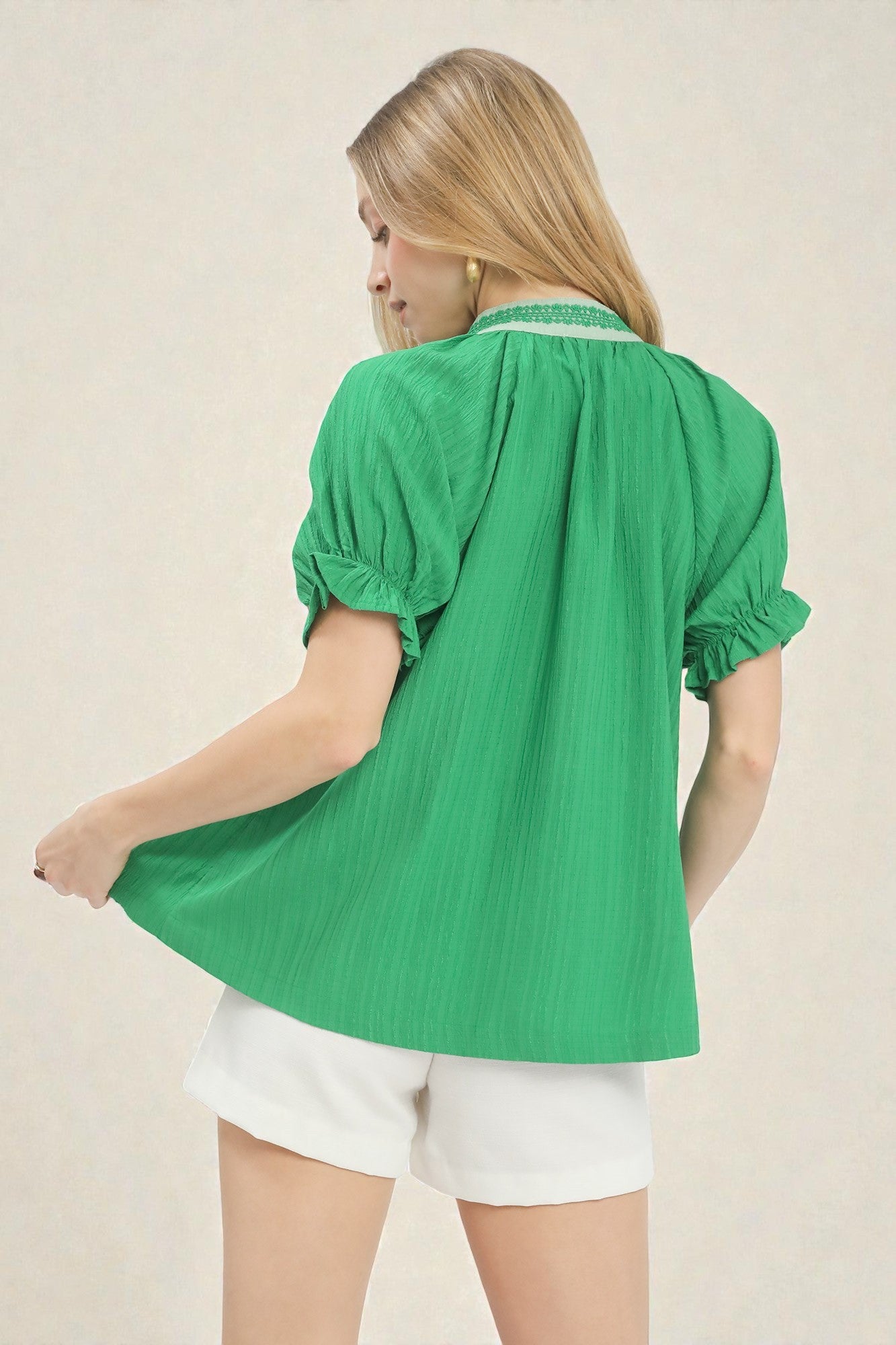 Woman wearing a green blouse and white shorts on a beige background