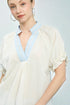 Woman wearing a white blouse with light blue trim on a plain background