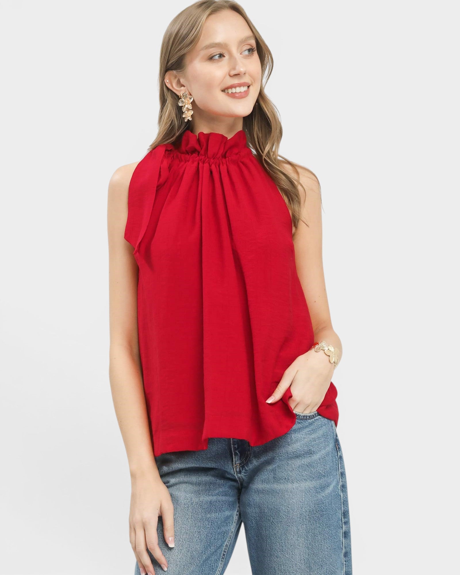 Woman wearing a red sleeveless top and blue jeans on a light gray background