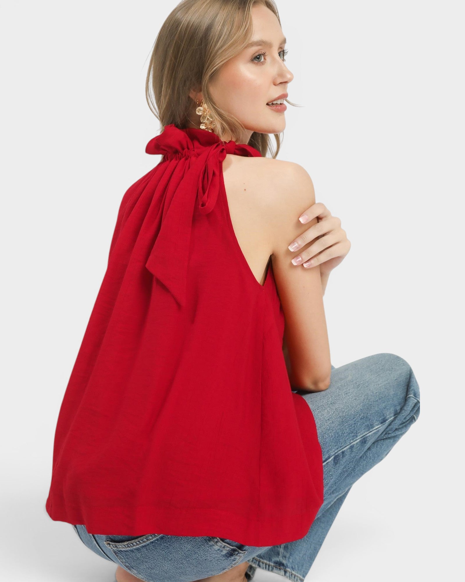 Woman wearing a red halter top and blue jeans on a white background