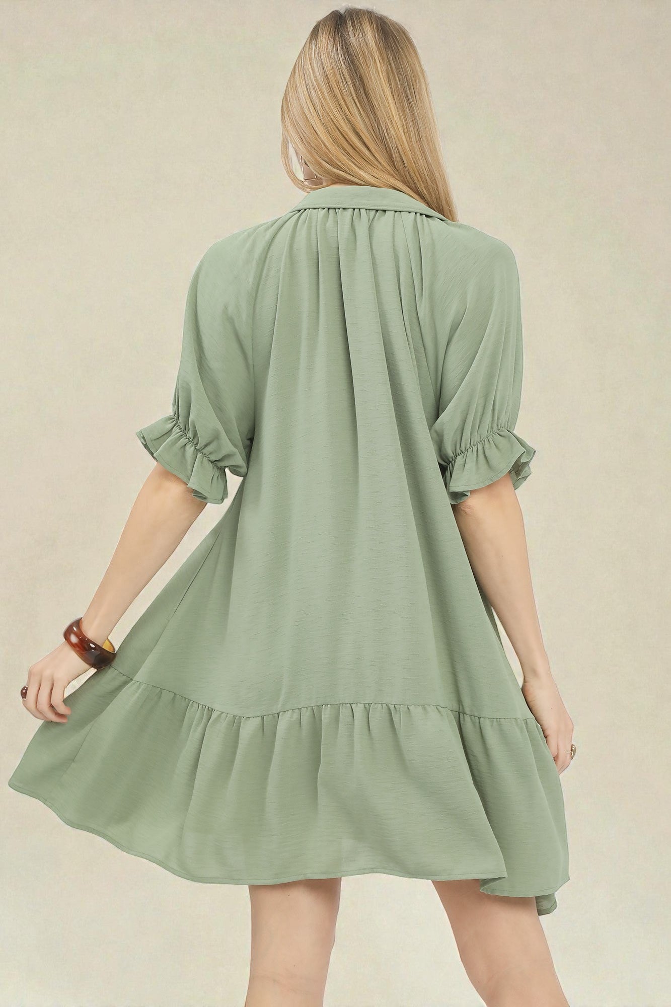 Woman wearing a green dress with ruffled layers on a beige background