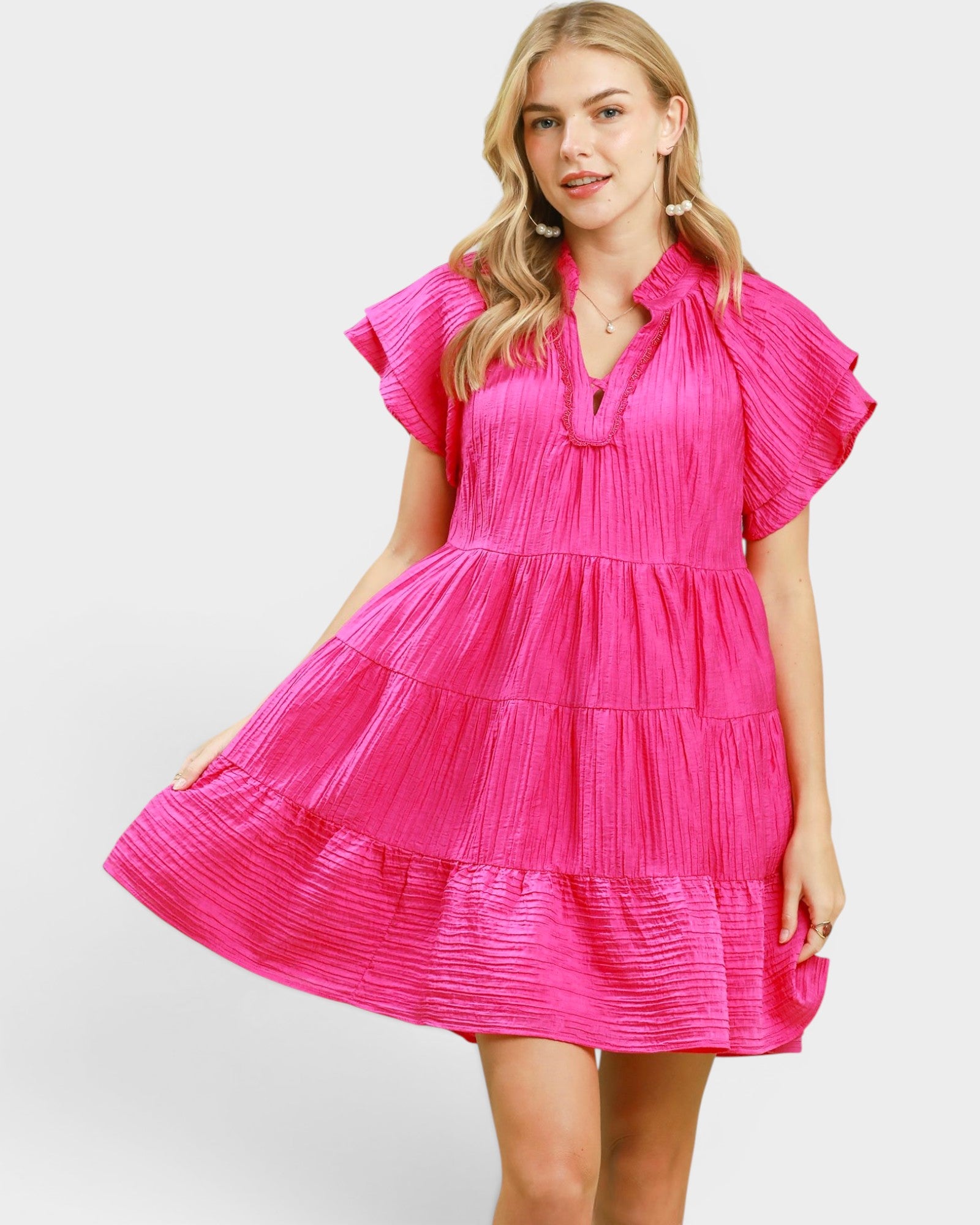 Woman wearing a bright pink dress with ruffled sleeves on a white background