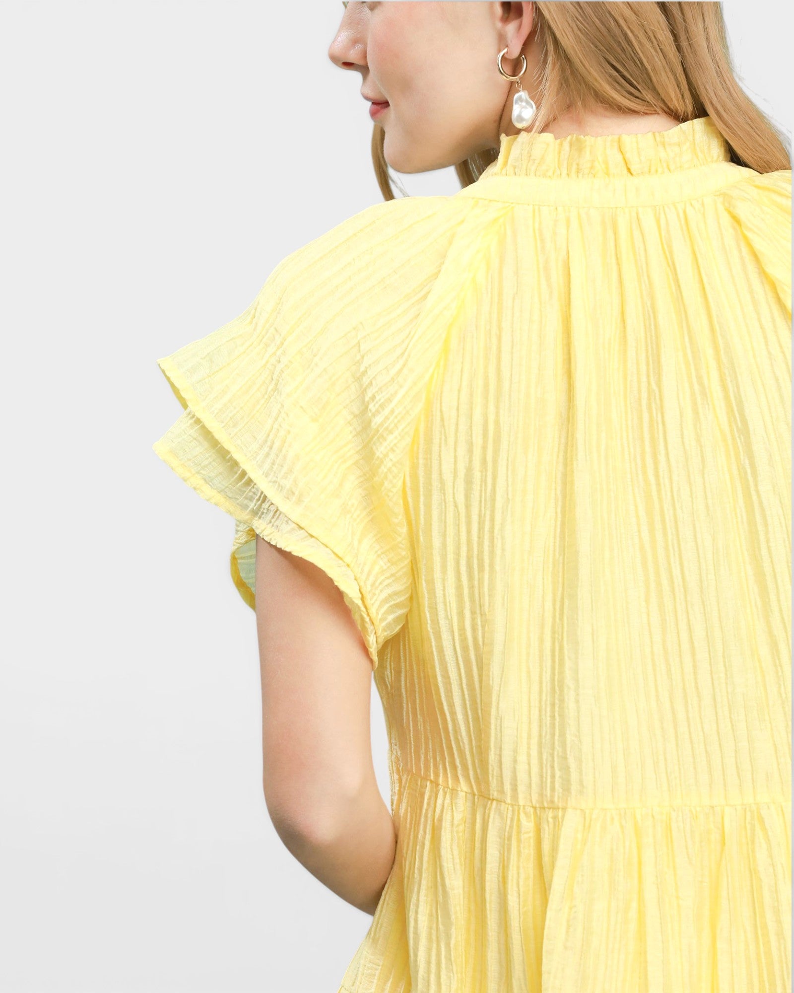 Yellow pleated dress worn by a person on a light gray background