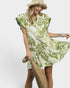 Woman wearing a green and white floral dress with a straw hat and bag on a white background