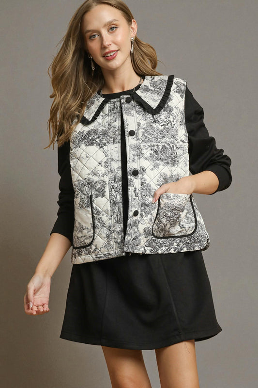 Woman wearing a black and white patterned vest over a black long-sleeve shirt and skirt on a gray background