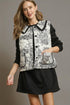 Woman wearing a black and white patterned vest over a black long-sleeve shirt and skirt on a gray background