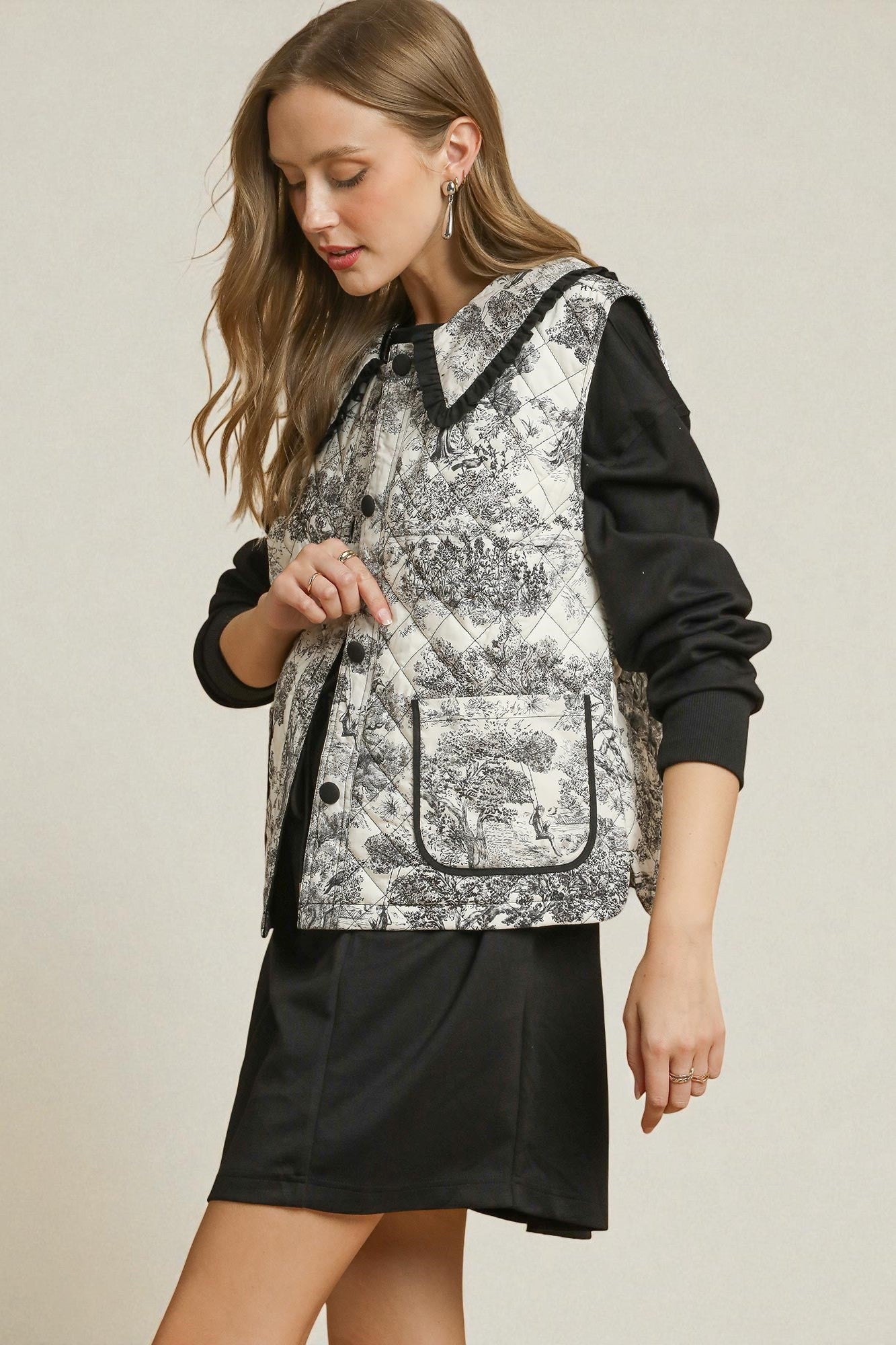 Woman wearing a black and white patterned vest over a black outfit on a beige background