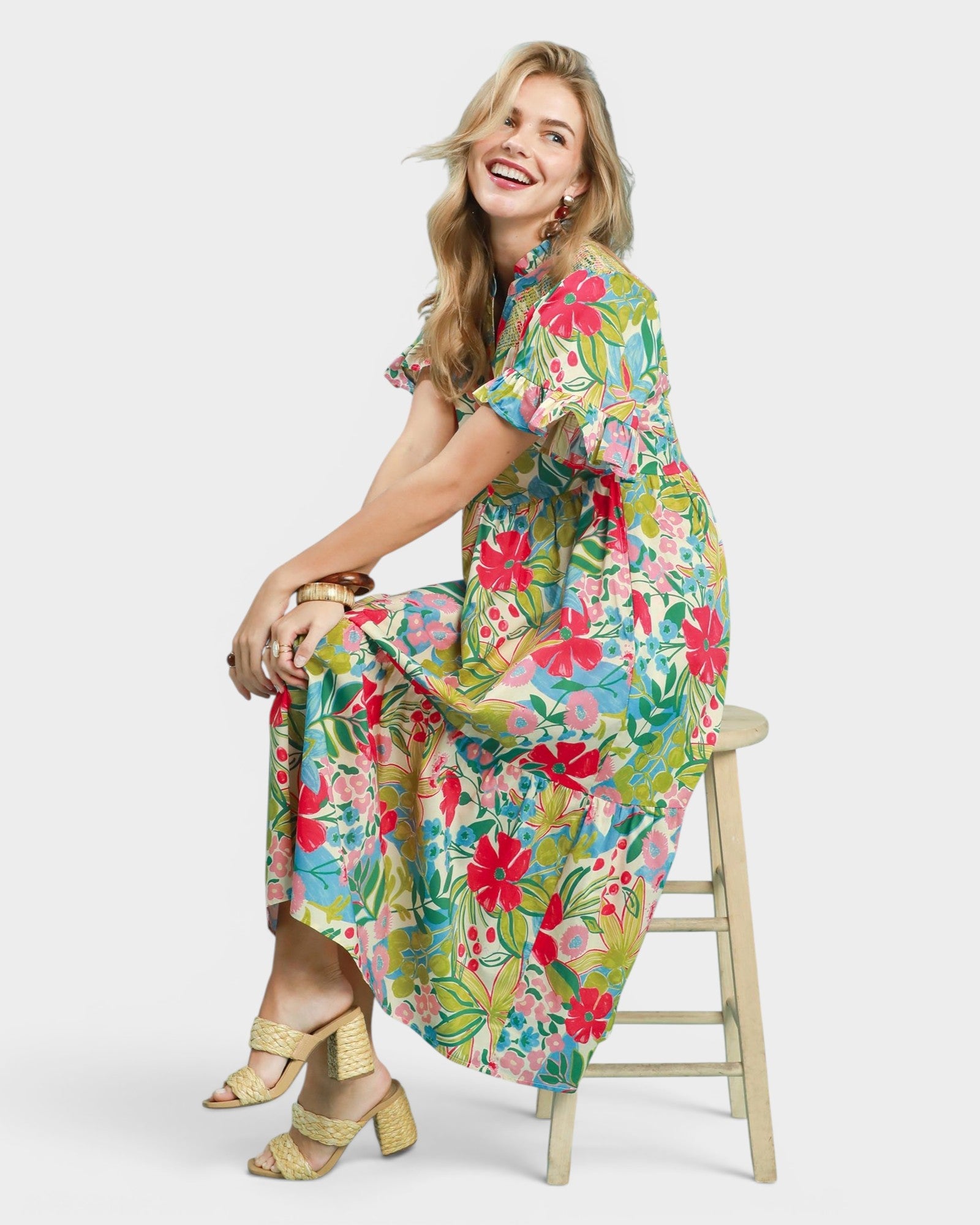 Woman wearing a colorful floral dress sitting on a stool against a white background