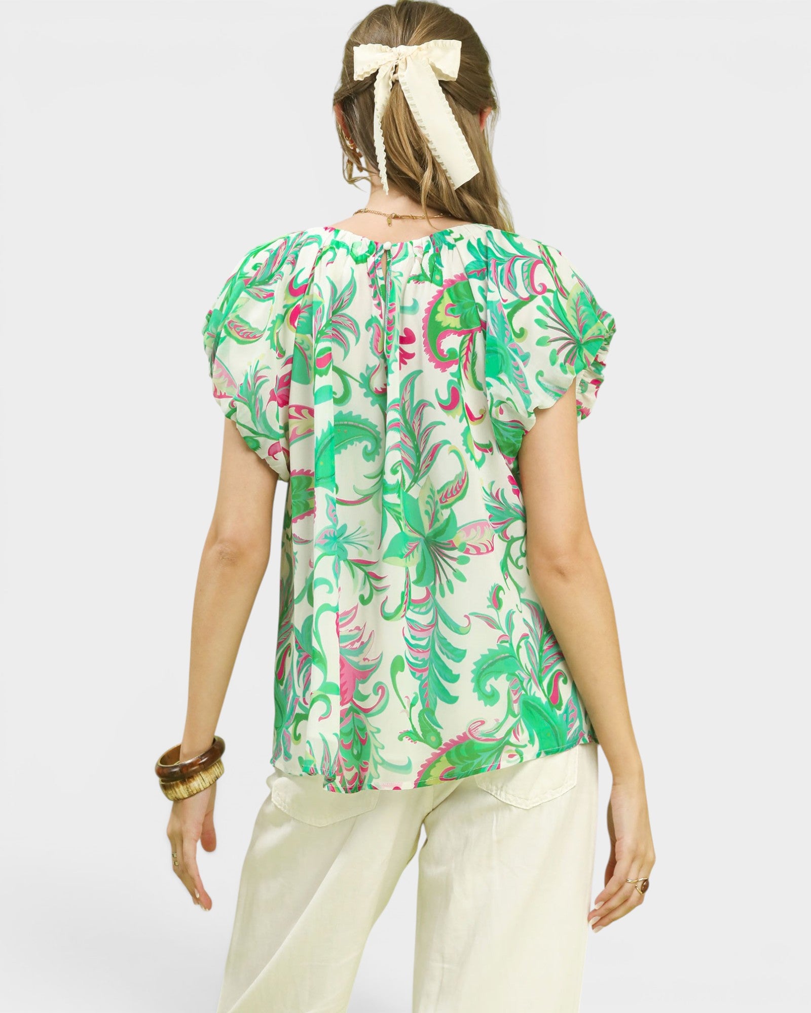 Woman wearing a green floral blouse with white pants on a plain background