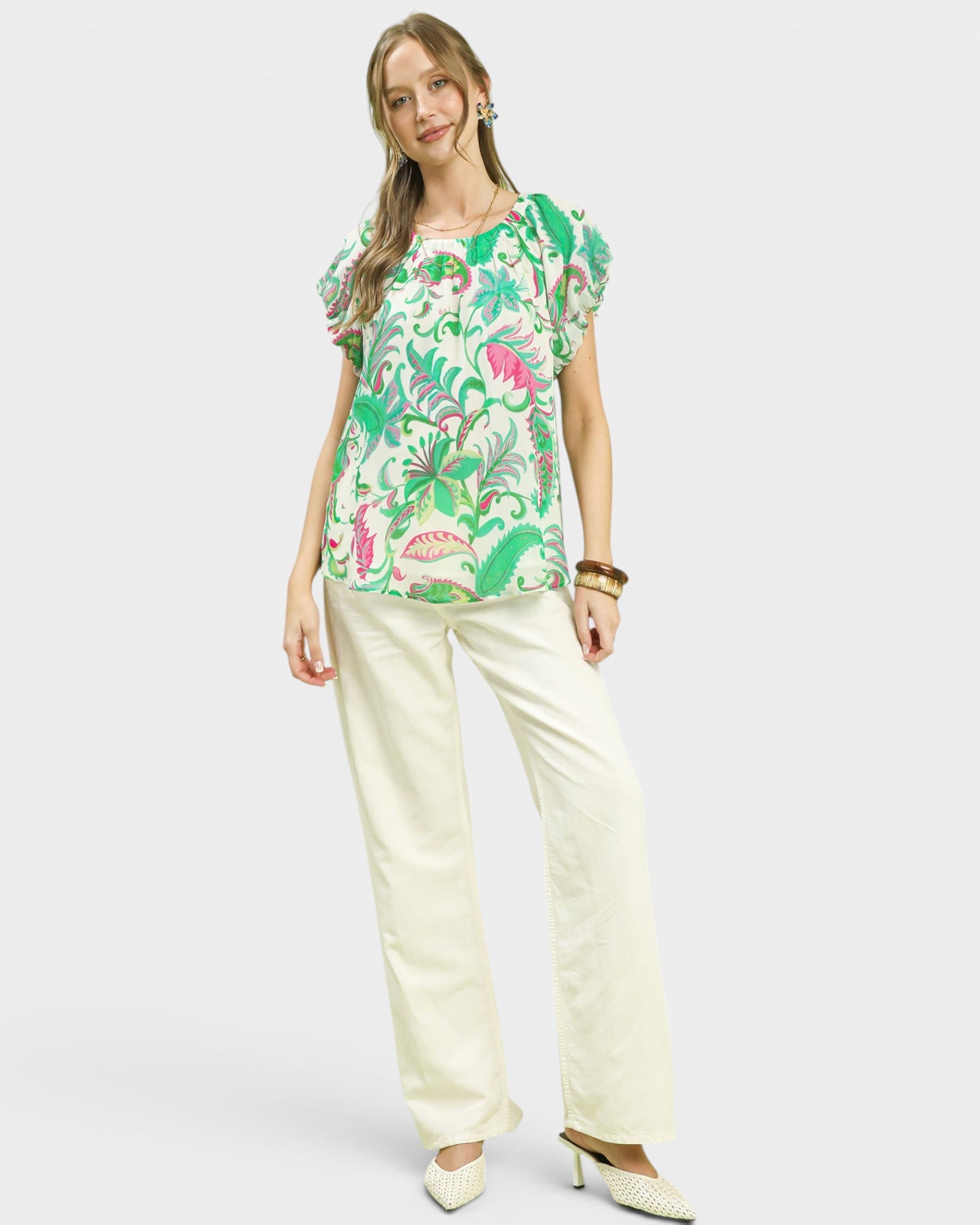 Woman wearing a colorful floral top and white pants on a white background
