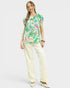 Woman wearing a colorful floral top and white pants on a white background