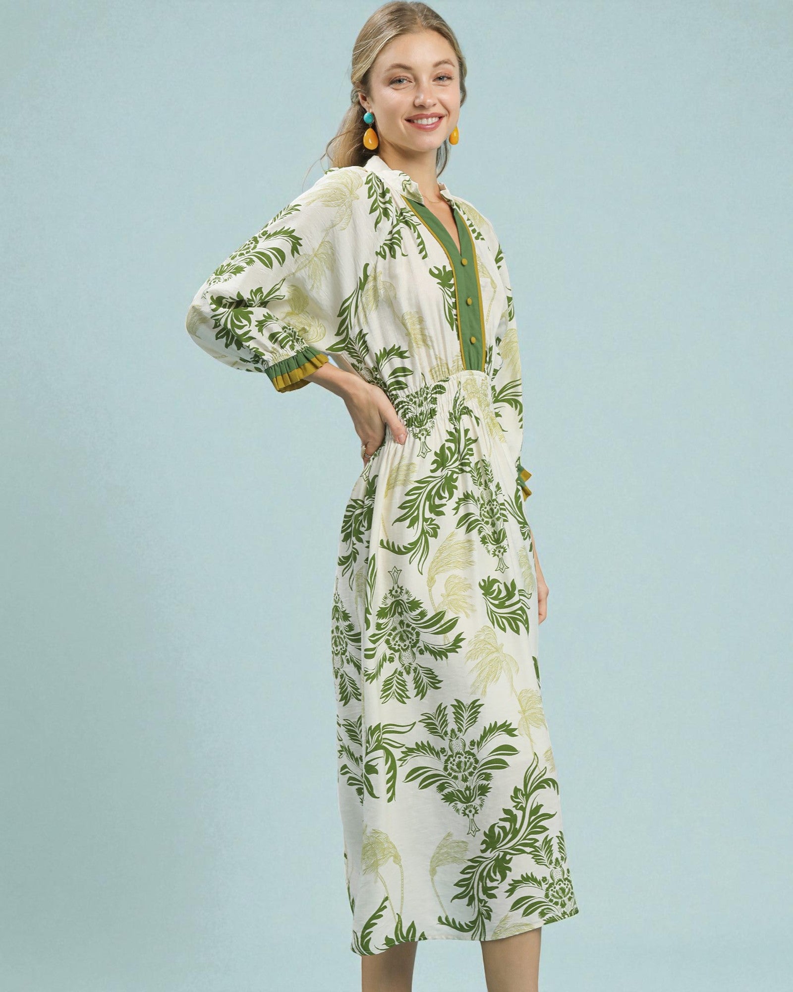 Woman wearing a white dress with green floral pattern against a light blue background