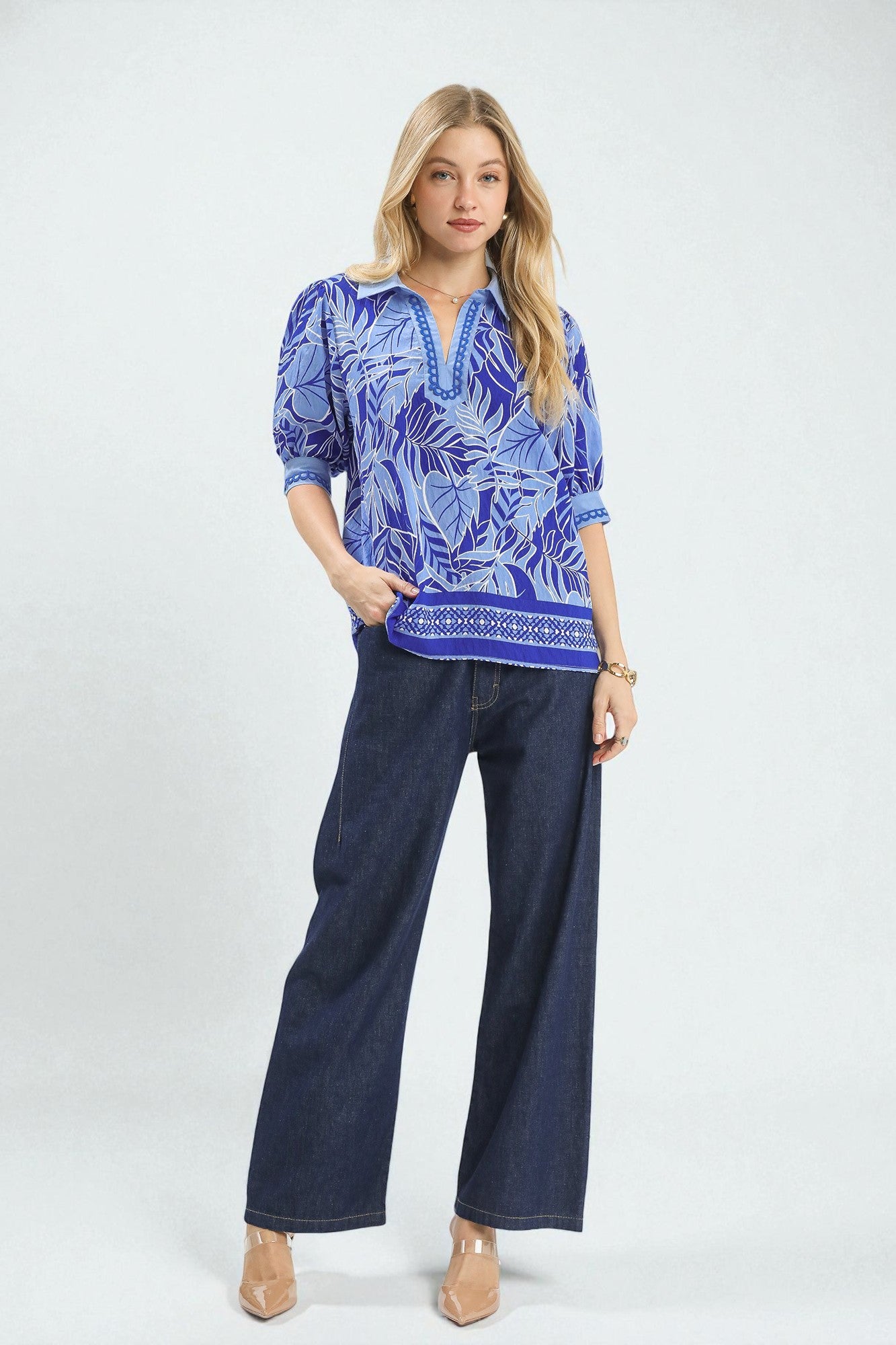 Woman wearing a blue patterned blouse and navy pants on a white background