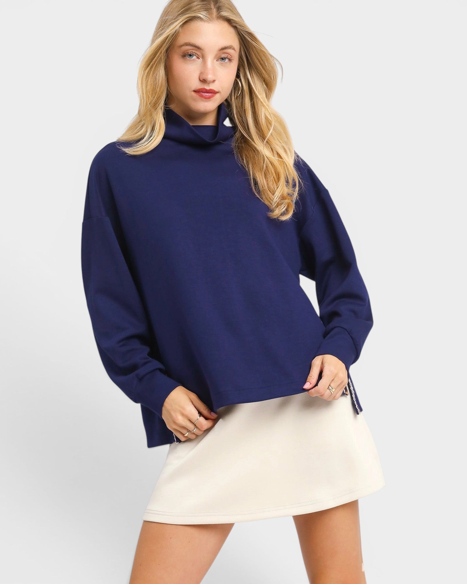 Woman wearing a navy blue sweater and white skirt on a light gray background