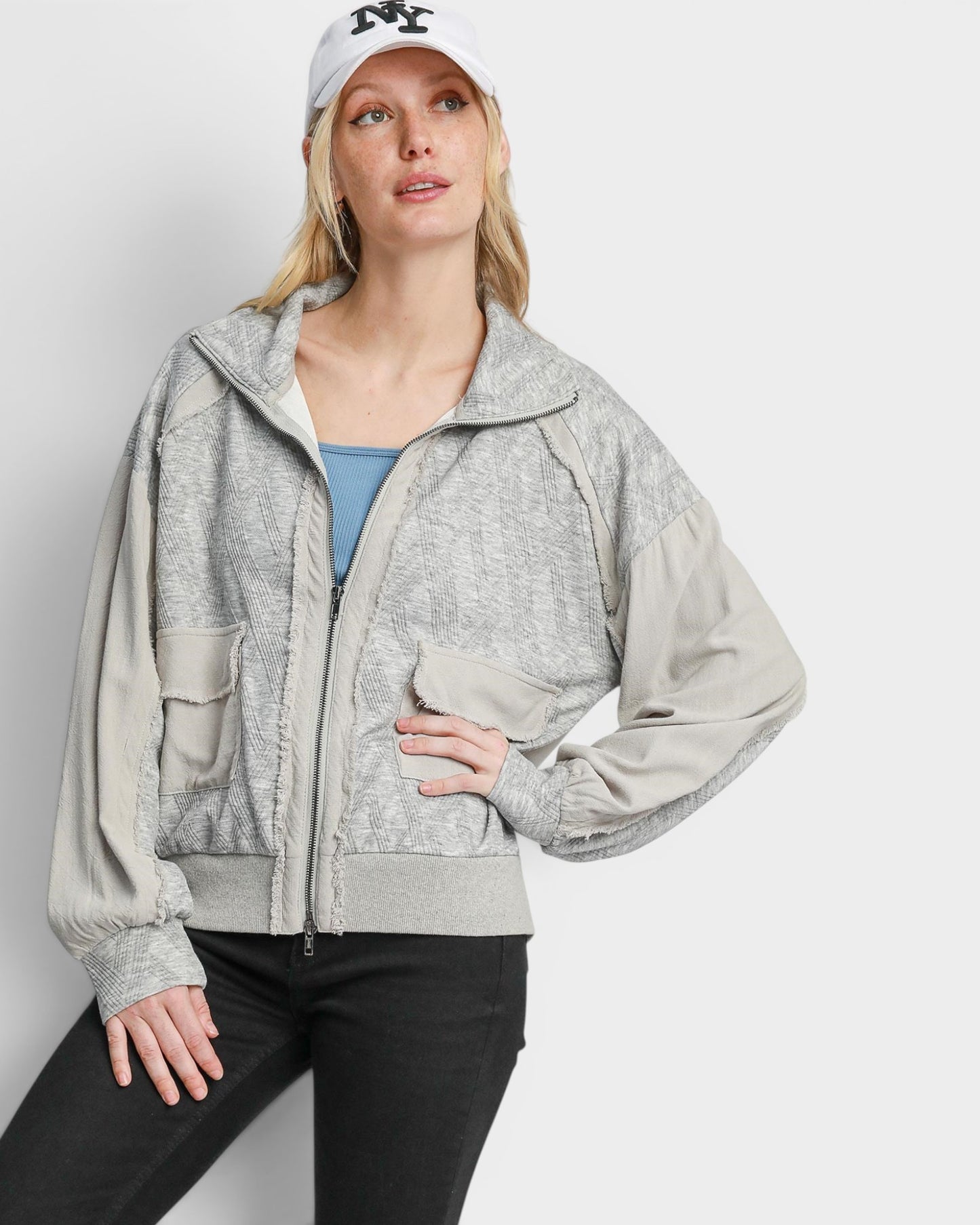 Woman wearing a gray zip-up hoodie and black pants on a white background