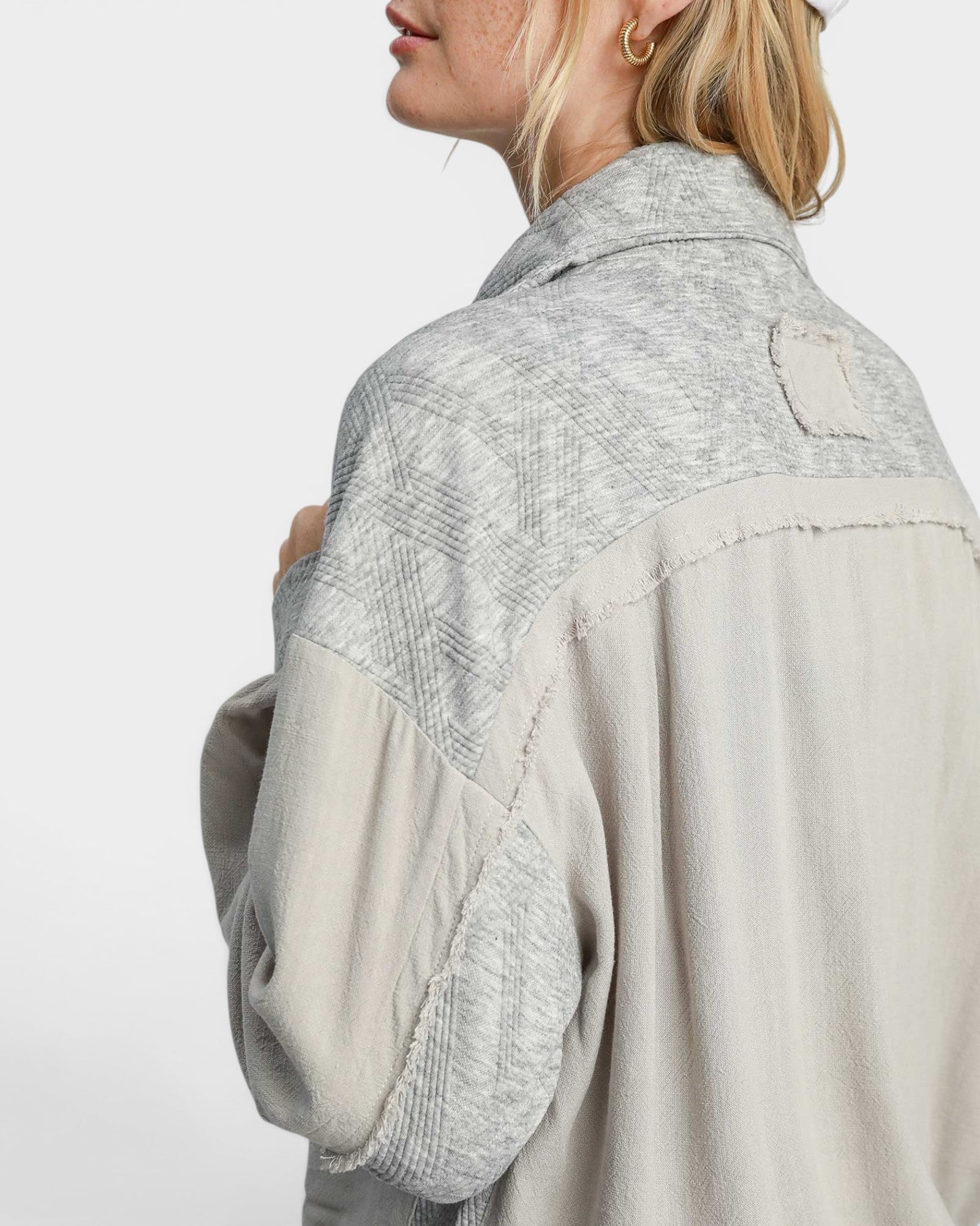 Person wearing a light gray and beige jacket with a white background