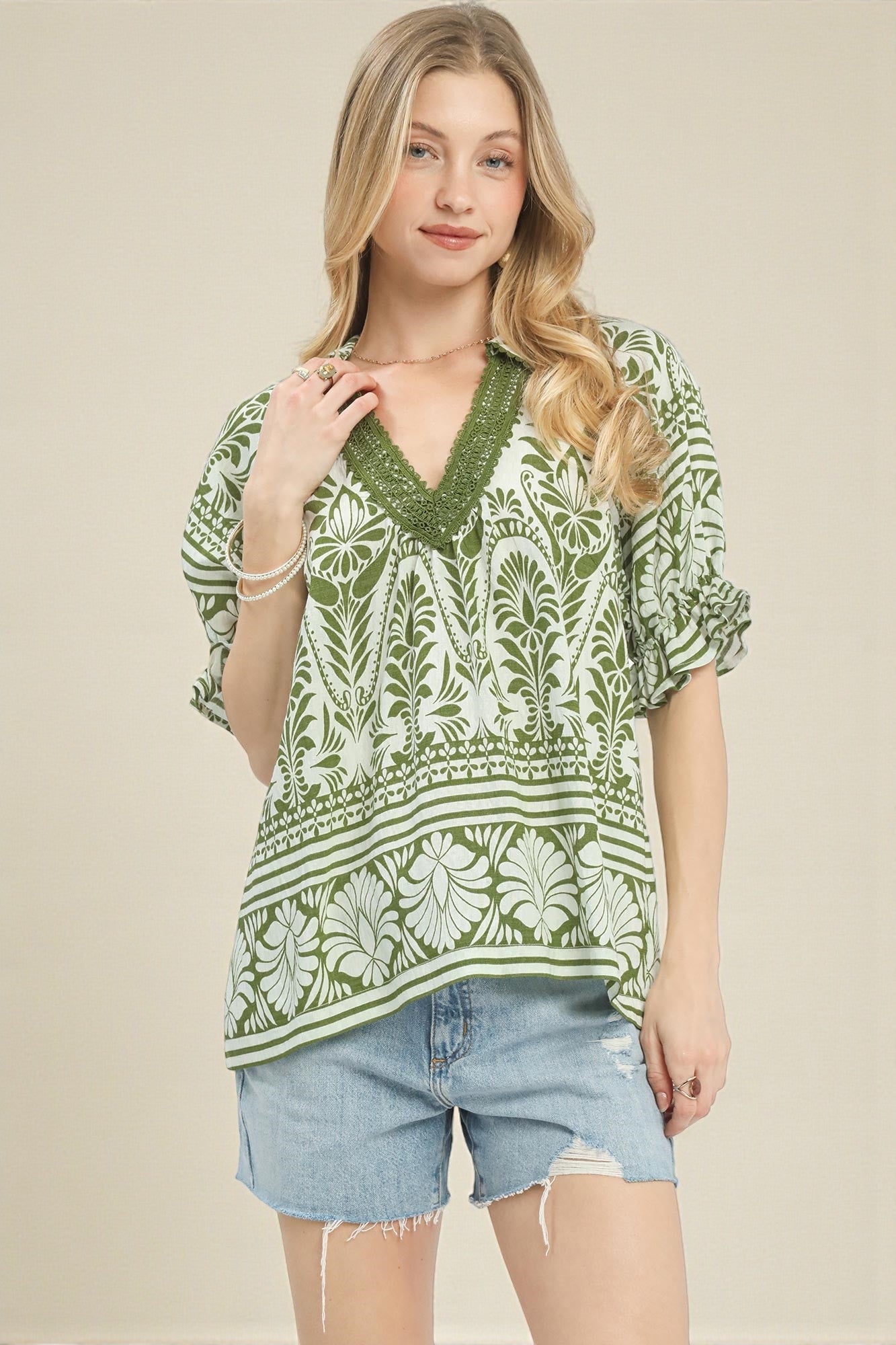 Woman wearing a green and white patterned top with denim shorts on a beige background