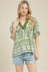 Woman wearing a green and white patterned top with denim shorts on a beige background
