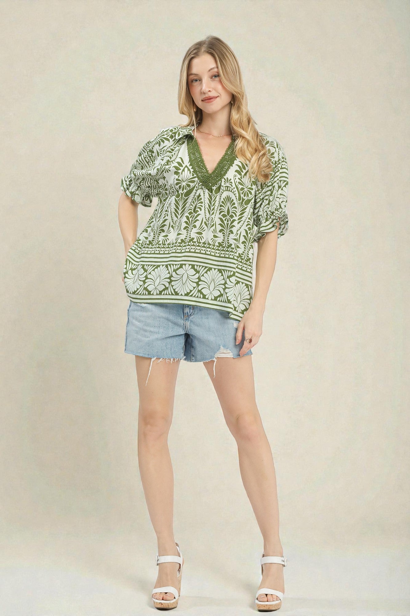 Woman wearing a green patterned top and denim shorts on a beige background