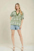 Woman wearing a green patterned top and denim shorts on a beige background