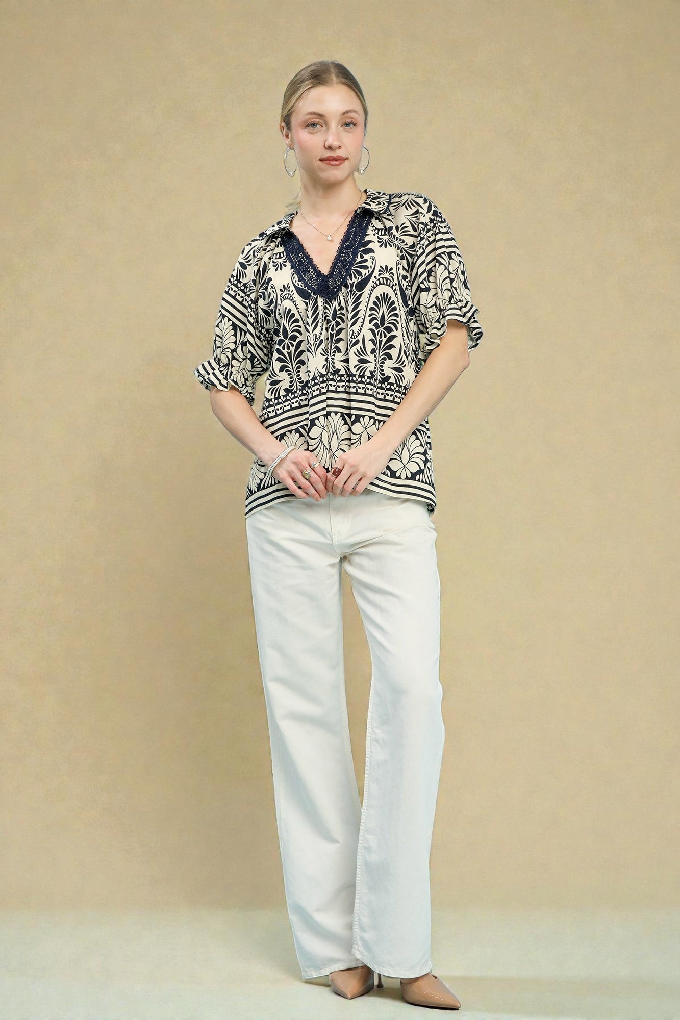 Woman wearing a patterned top and white pants against a beige background