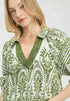 Woman wearing a green and white patterned blouse against a plain background
