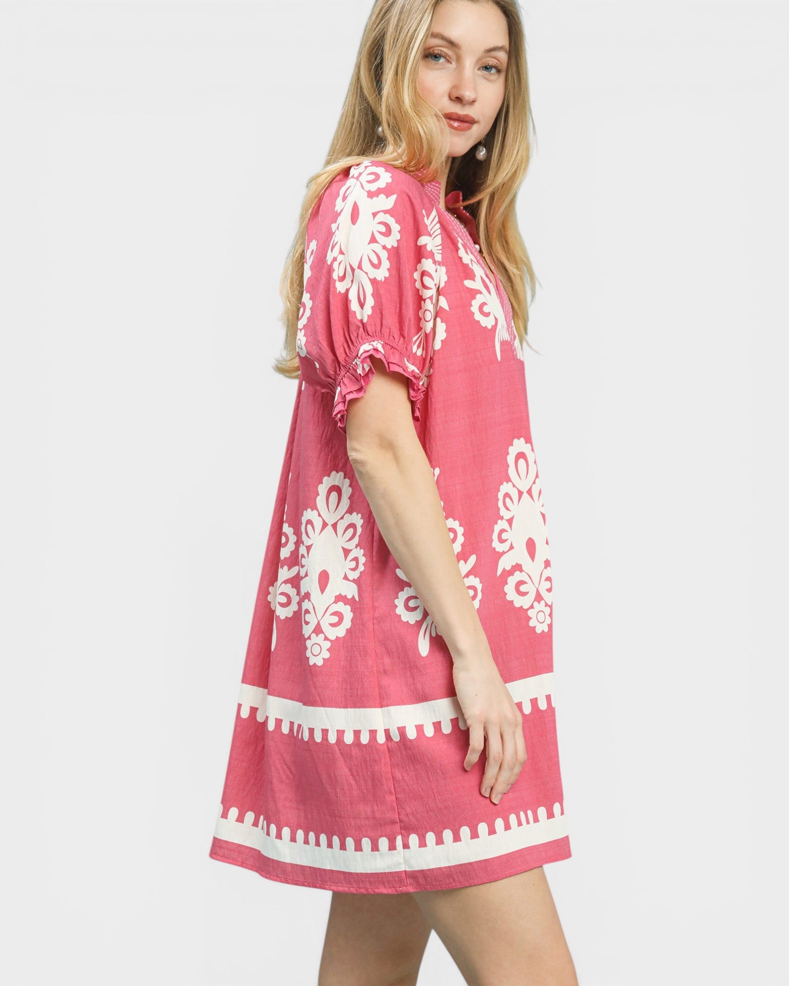 Woman wearing a pink dress with white patterns on a white background