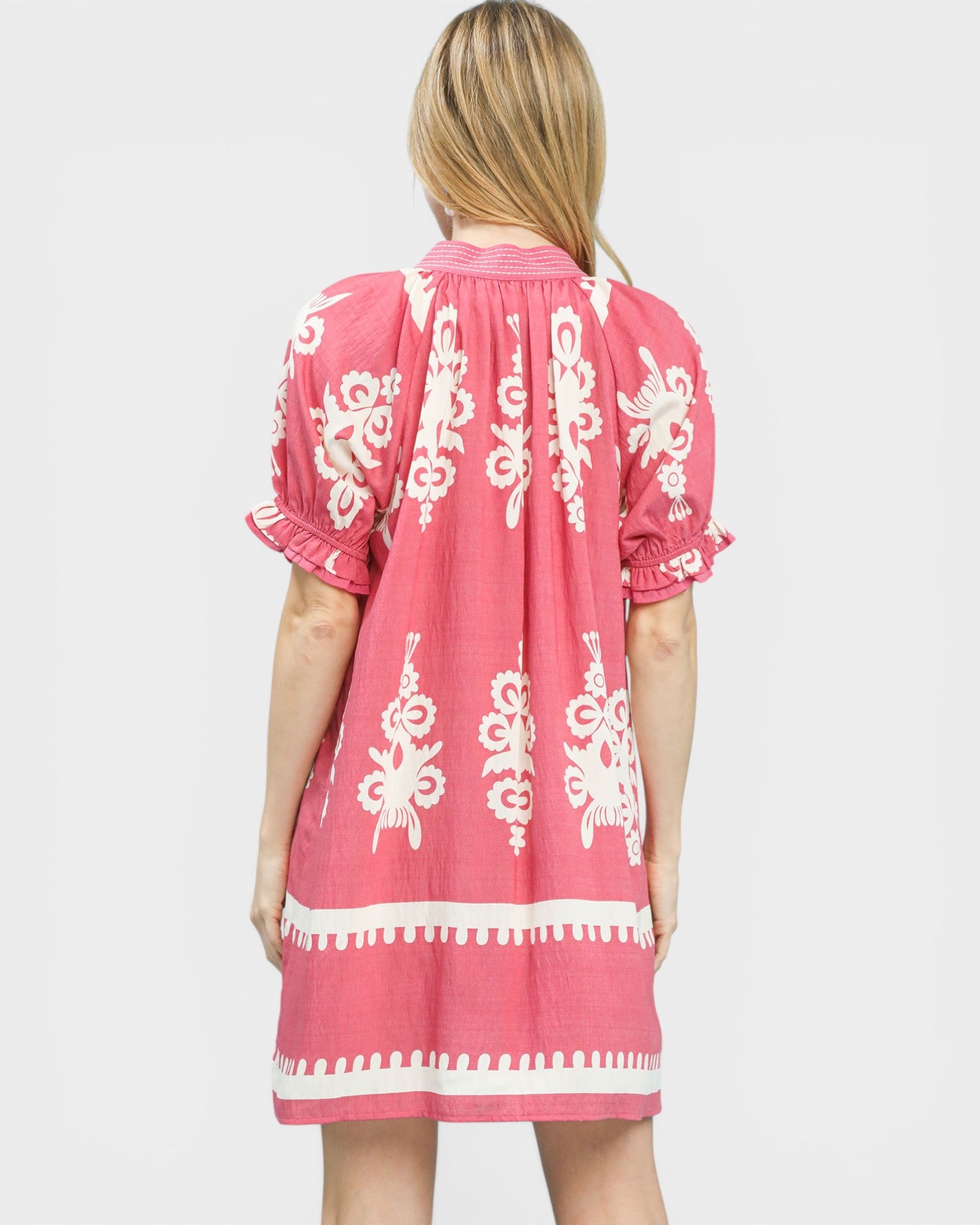 Woman wearing a pink dress with white patterns on a white background