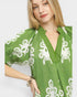 Woman wearing a green dress with white floral patterns on a plain background