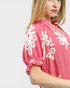 Woman wearing a pink dress with white floral embroidery on a plain background