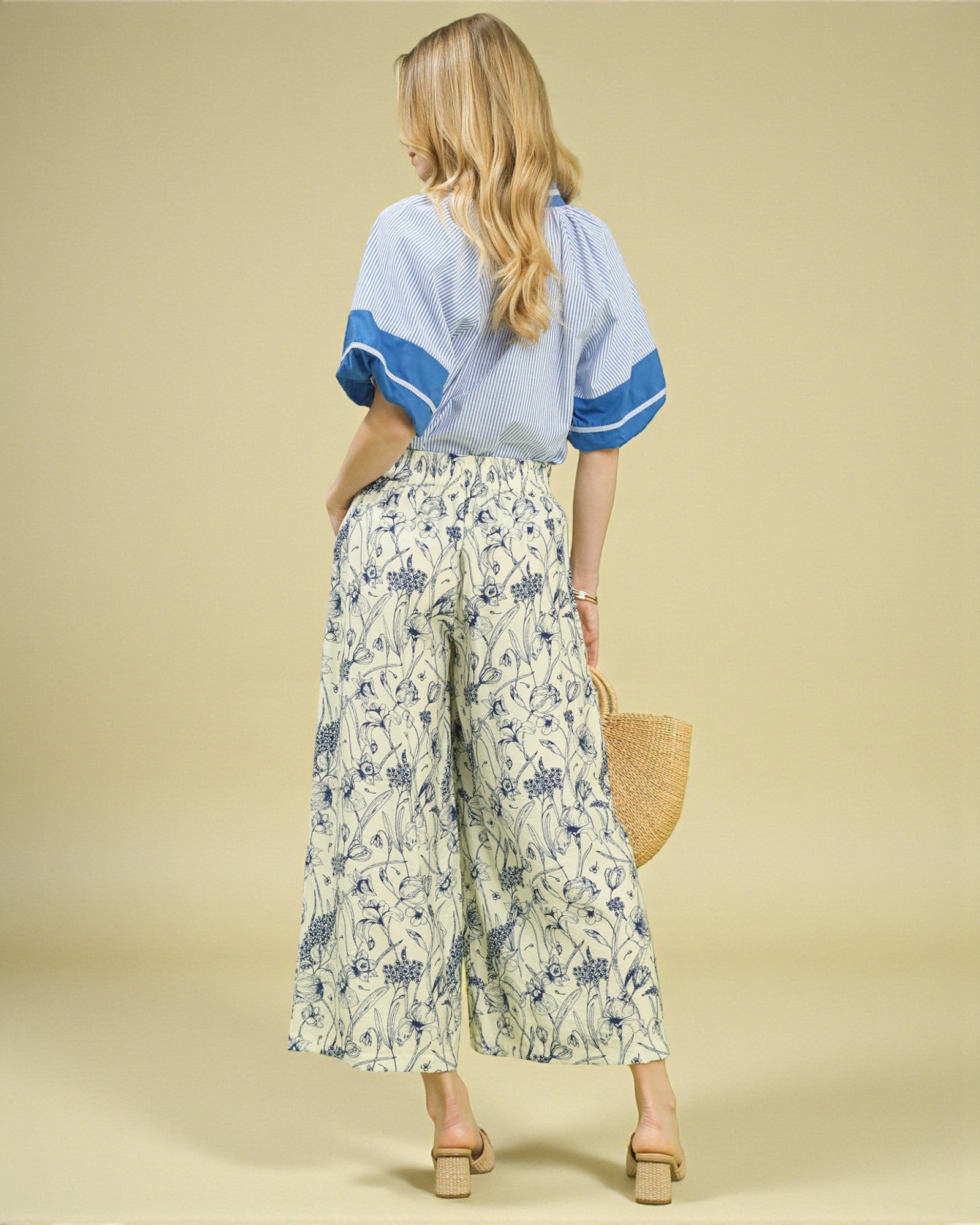 Woman wearing a light blue top with blue sleeves and floral pants on a beige background
