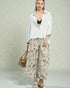 Woman wearing a white shirt, black top, and patterned pants with a beige bag on a light background