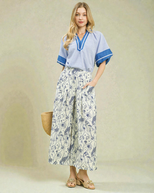 Woman wearing a light blue top and floral pants with a beige background