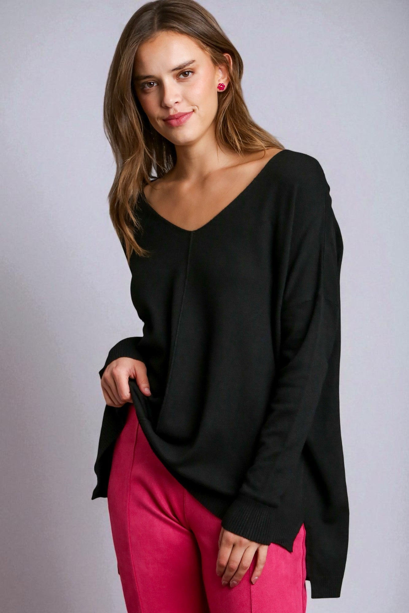 Woman wearing a black top and pink pants against a gray background