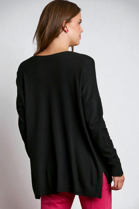 Person wearing a black cardigan over pink pants on a plain background