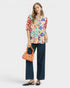 Woman wearing a colorful floral blouse and dark pants, holding an orange bag on a white background