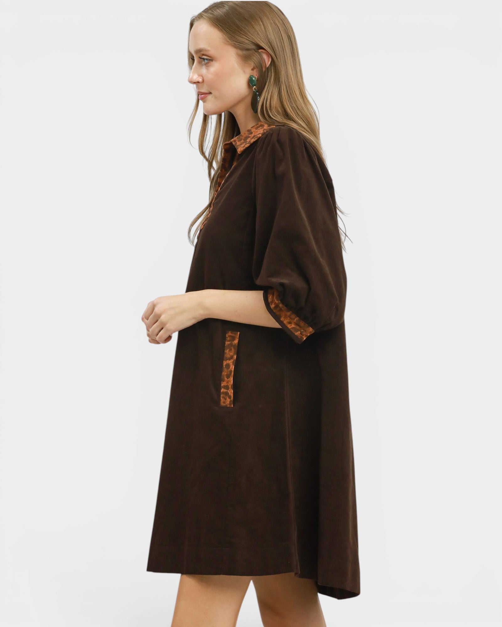 Woman wearing a brown dress with patterned trim on a white background