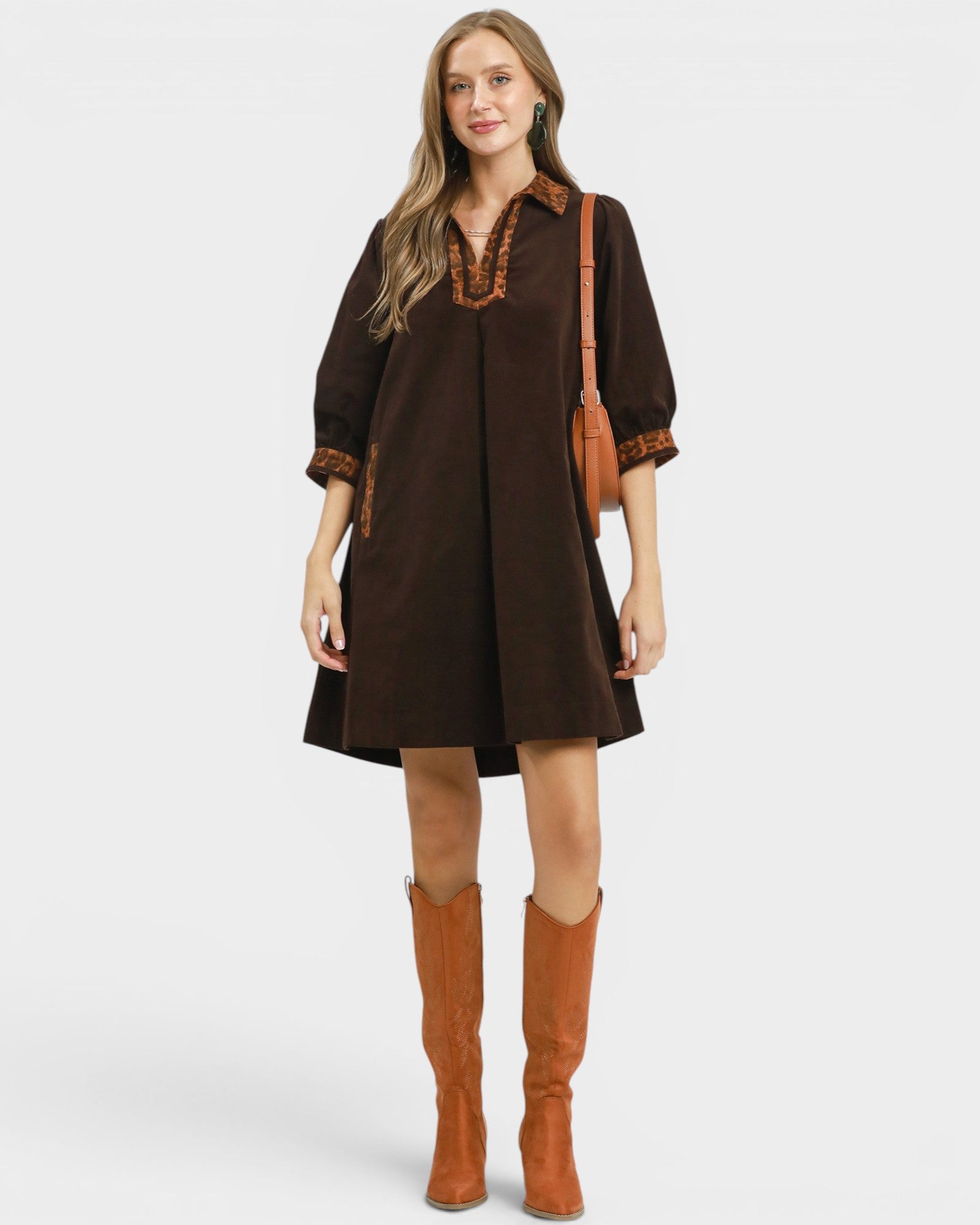 Woman wearing a brown dress with decorative trim and brown boots on a white background