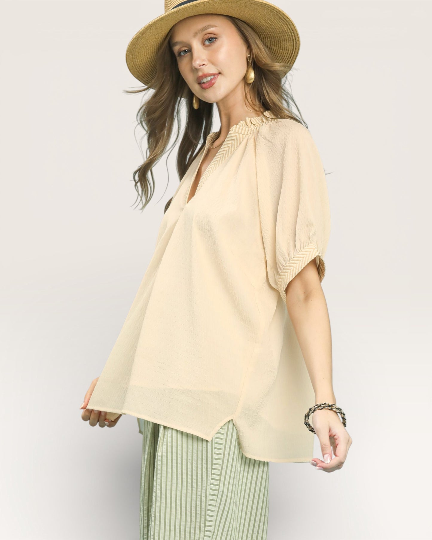 Woman wearing a beige blouse and green pants with a straw hat on a white background